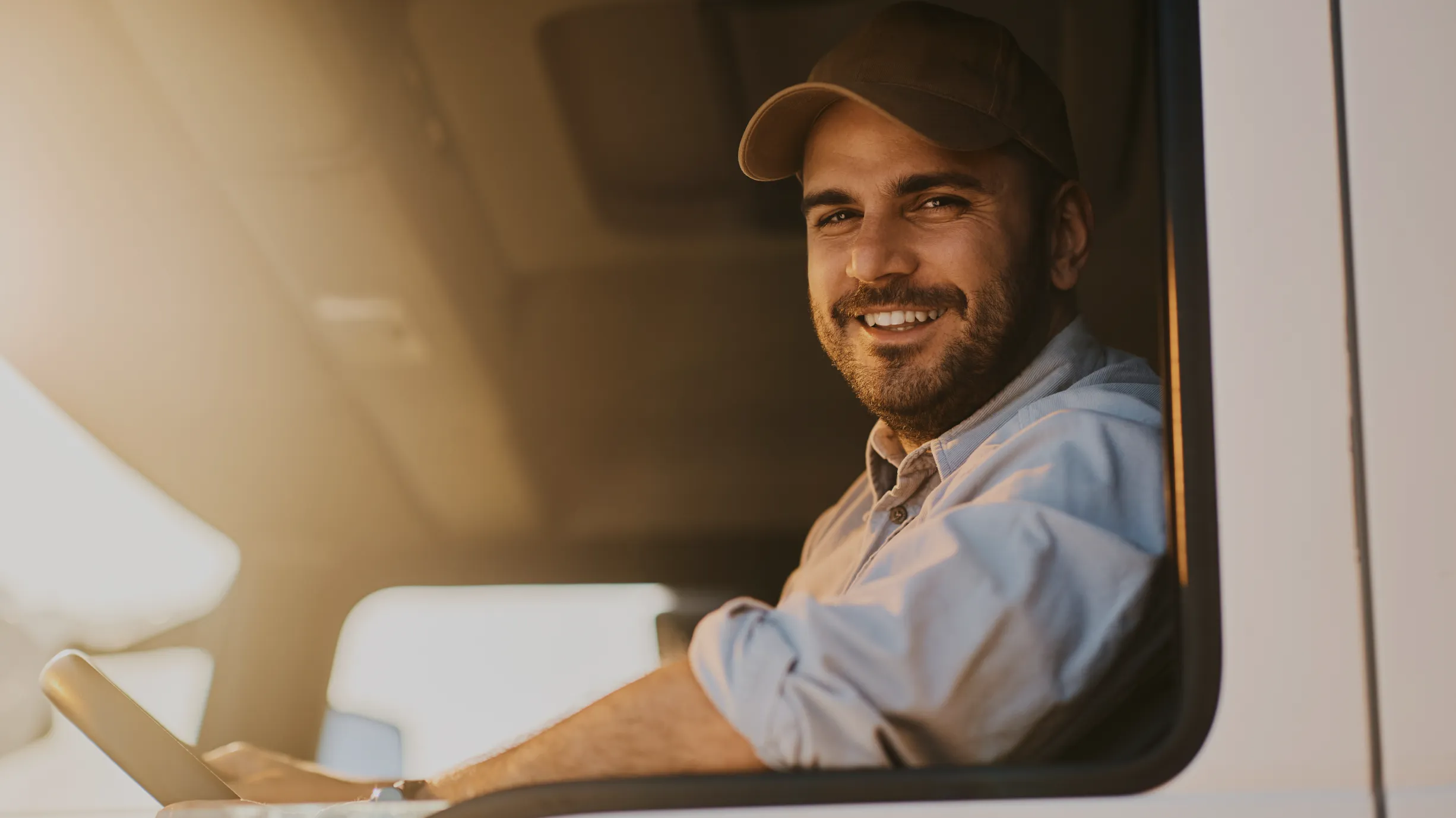 Un livreur souriant, casquette sur la tête, au volant de sa camionnette, accoudé à la fenêtre ouverte