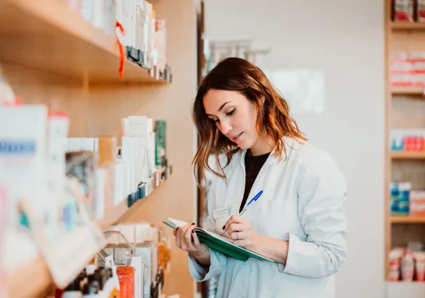Pharmacienne relevant son stock devant les rayonnages de l’officine