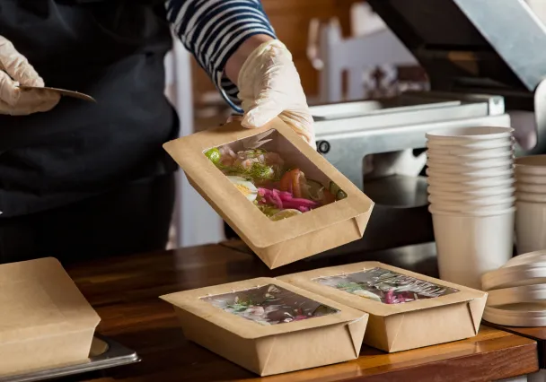 Mains gantées refermant une barquette repas à fenêtre