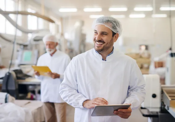 Responsable de production en tenue d’hygiène consultant sa tablette en cuisine centrale