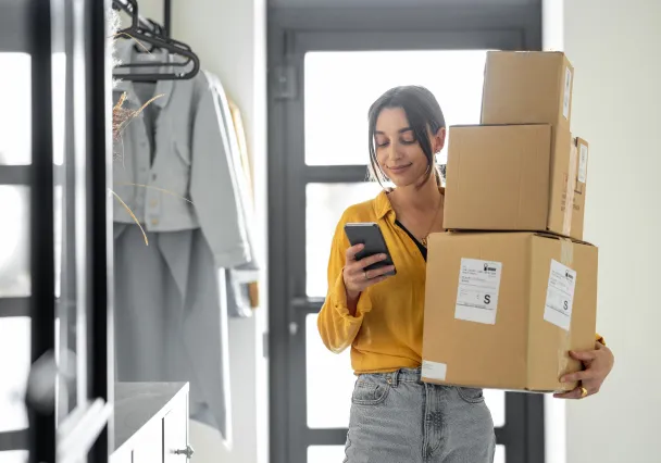 Cliente consultant son téléphone en portant une pile de colis à son domicile