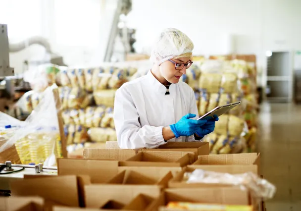 Opératrice en tenue d’hygiène contrôlant des cartons sur une ligne de conditionnement alimentaire