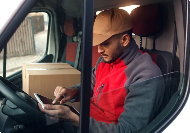Un livreur au volant de sa camionnette, son téléphone à la main