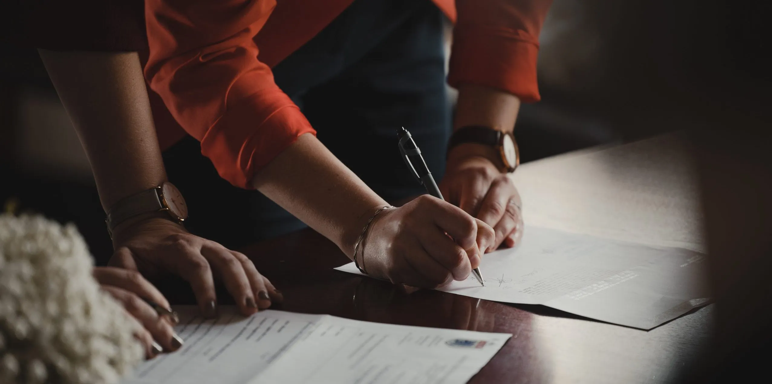 Gros plan sur deux paires de mains à un bureau : l’une signe un document au stylo