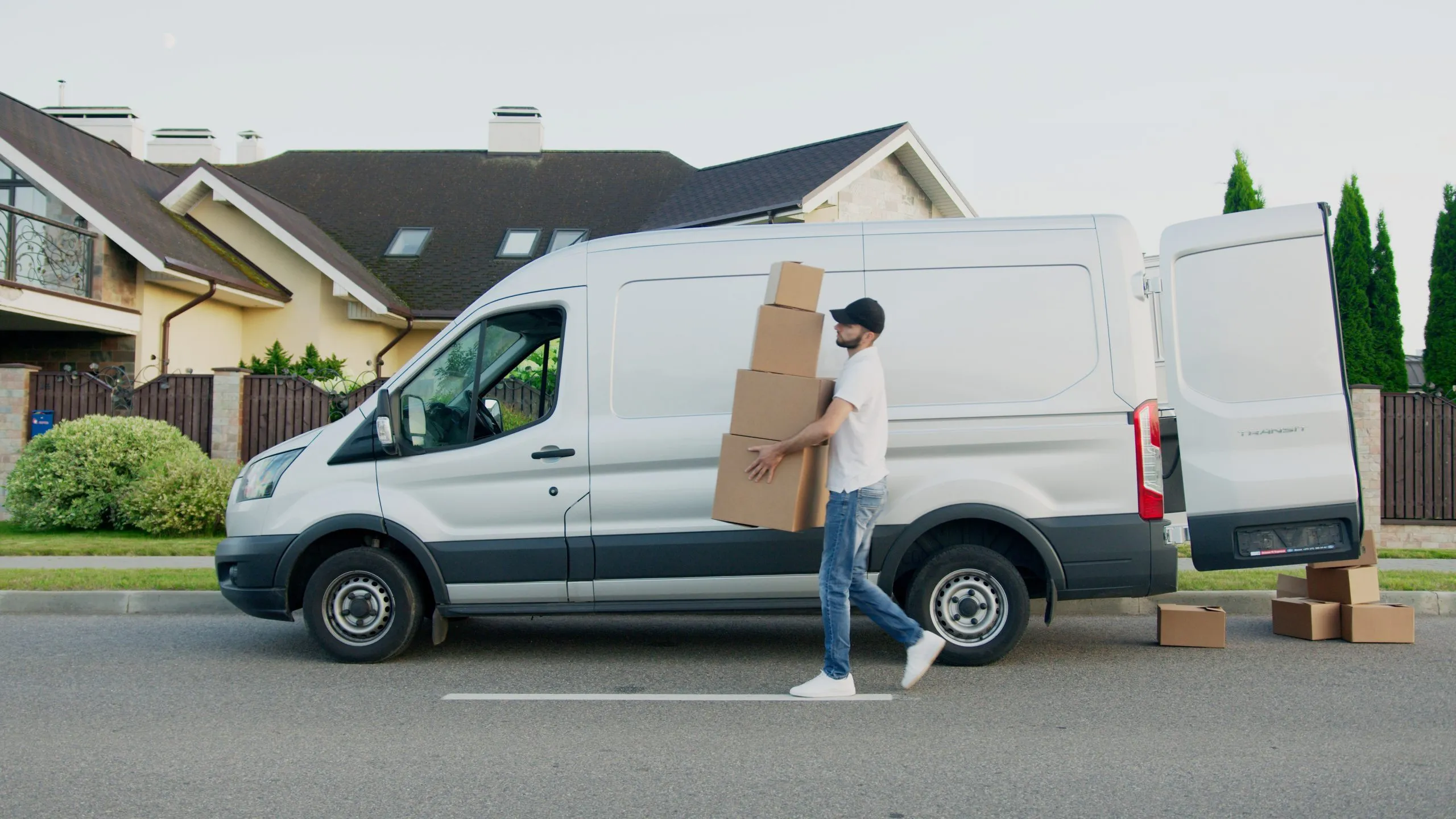Livreur en camionnette qui porte des caisses en carton dans une rue résidentielle.